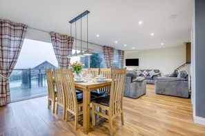 A spacious living room with a dining area, large windows, a grey sofa, and a flat-screen TV. - 4 Bed in Winnards Perch (oc-w34023) (Winnard's Perch)