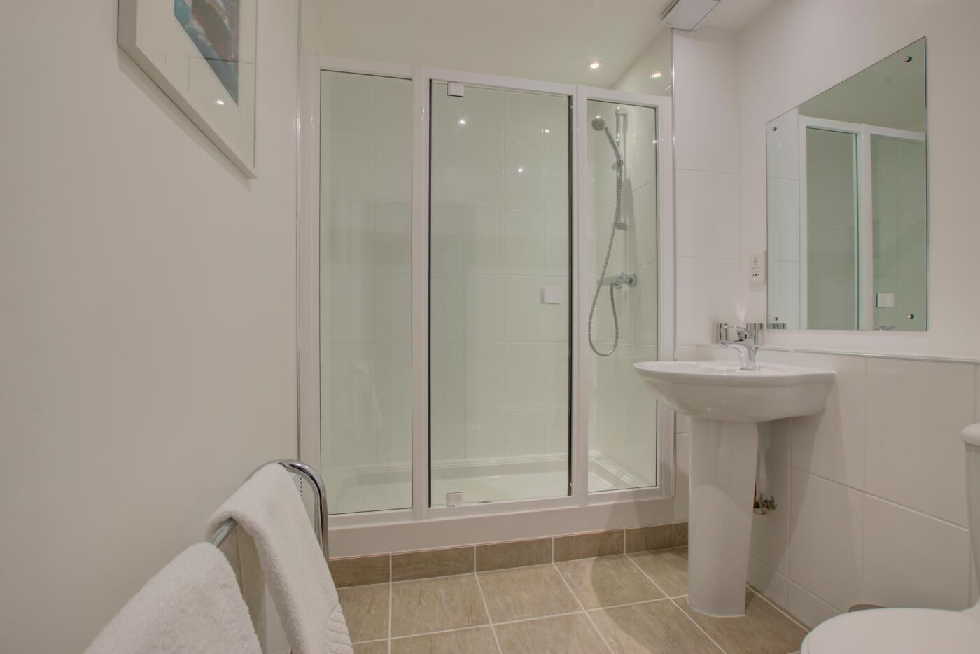 A modern bathroom with a glass-enclosed shower, a pedestal sink, and a large mirror.