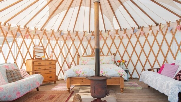 A cozy yurt interior with a central bed, a wooden dresser, and a rustic stove.