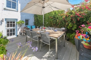 Eine Terrasse im Freien mit Tisch und Stühlen, umgeben von üppiger Bepflanzung und blühenden Pflanzen.