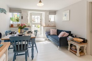 A dining area with a wooden table and blue chairs, a dark blue sofa with striped pillows, and a small side table with a bowl. - 2 Bed in Mousehole (oc-seahor) (Mousehole)