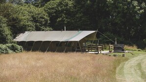 Een tentvormige accommodatie met een overdekt terras en een picknicktafel.