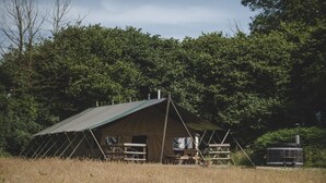 Een tent met dak, omringd door een veld en bomen.