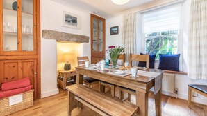 A cozy room with a wooden dining table, benches, a lamp, and a window with curtains. - 3 Bed in Porthleven (oc-harbli) (Porthleven)