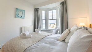 A neatly made bed with a beige quilt, pillows, and folded towels. - 3 Bed in Porthleven (oc-harbli) (Porthleven)