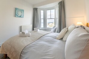 A neatly made bed with a beige quilt, pillows, and folded towels. - 3 Bed in Porthleven (oc-harbli) (Porthleven)