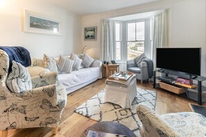A living room with a sofa, armchairs, a coffee table, a TV, and a bay window. - 3 Bed in Porthleven (oc-harbli) (Porthleven)