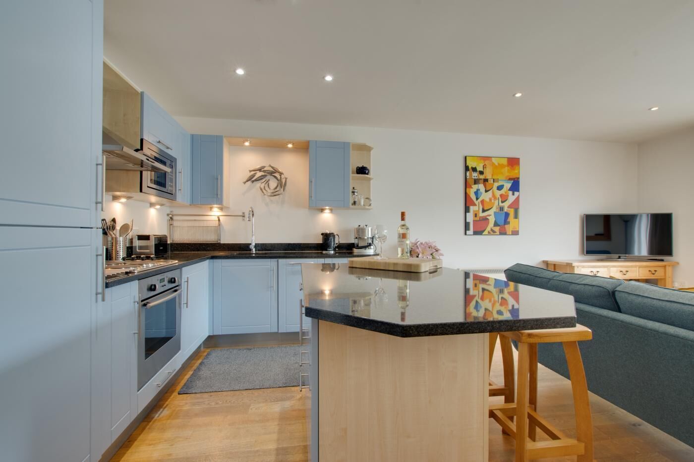 A modern kitchen with a central island, built-in appliances, and a dining area with a sofa and TV.