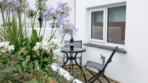 Pieni patio, jossa on pöytä ja tuoleja, ja jonka ympärillä on monenlaisia kasveja ja kukkia.