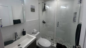 Un baño moderno con ducha de vidrio, lavamanos blanco y un inodoro.