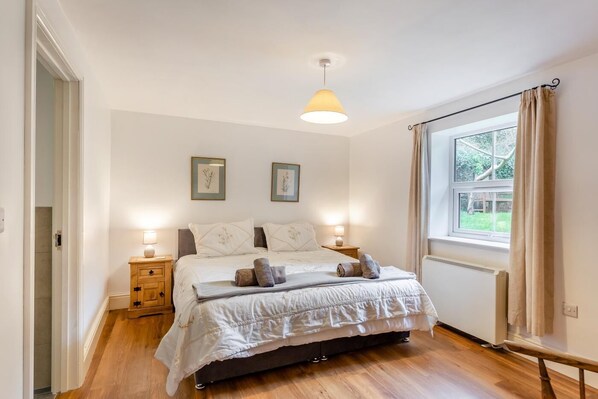 A bedroom with a bed, bedside lamps, a window with curtains, and framed pictures on the wall. - 4 Bed in Stokenham (oc-i34021) (Stokenham)