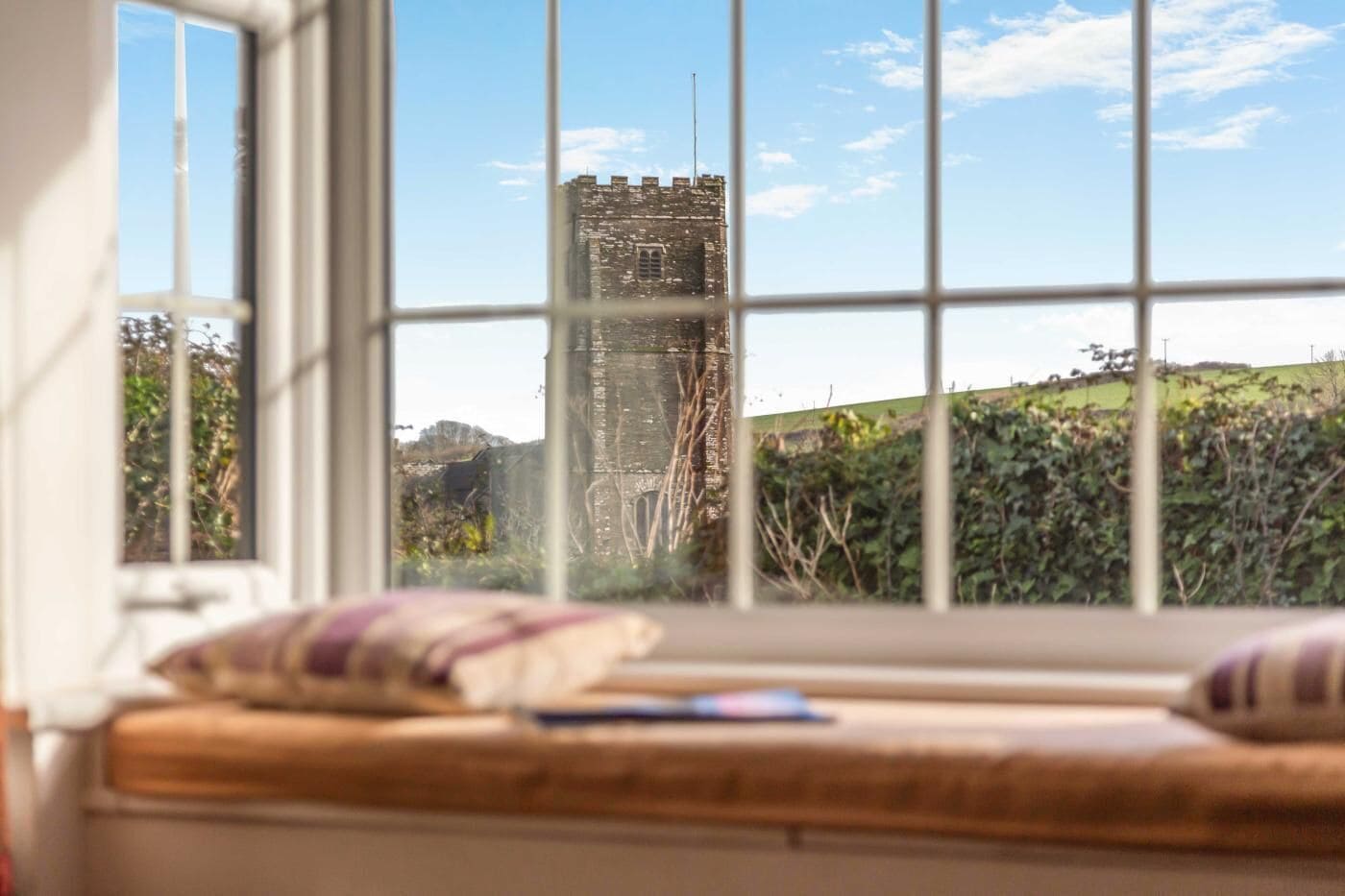 A view through a window with a stone tower in the background, a wooden bench, and a cushion.