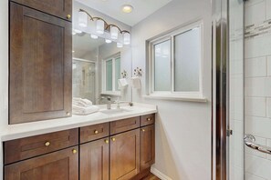 A modern bathroom with a large mirror, wooden vanity, white countertop, and a glass shower enclosure. - Family Favorite with Large Yard and BBQ (Fort Bragg)