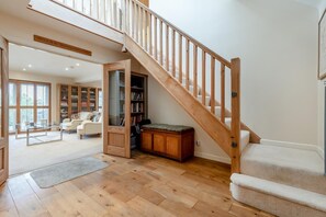 Ein geräumiger Wohnbereich mit einer Holztreppe, einer Glastür zum Balkon und einer gemütlichen Sitzecke mit Bücherregal.