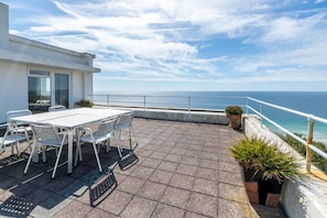 A terrace with a table and chairs, a potted plant, and a view of the sea.