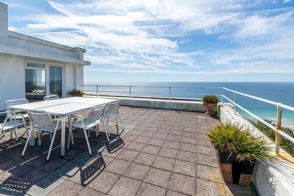 A terrace with a table and chairs, a potted plant, and a view of the sea.
