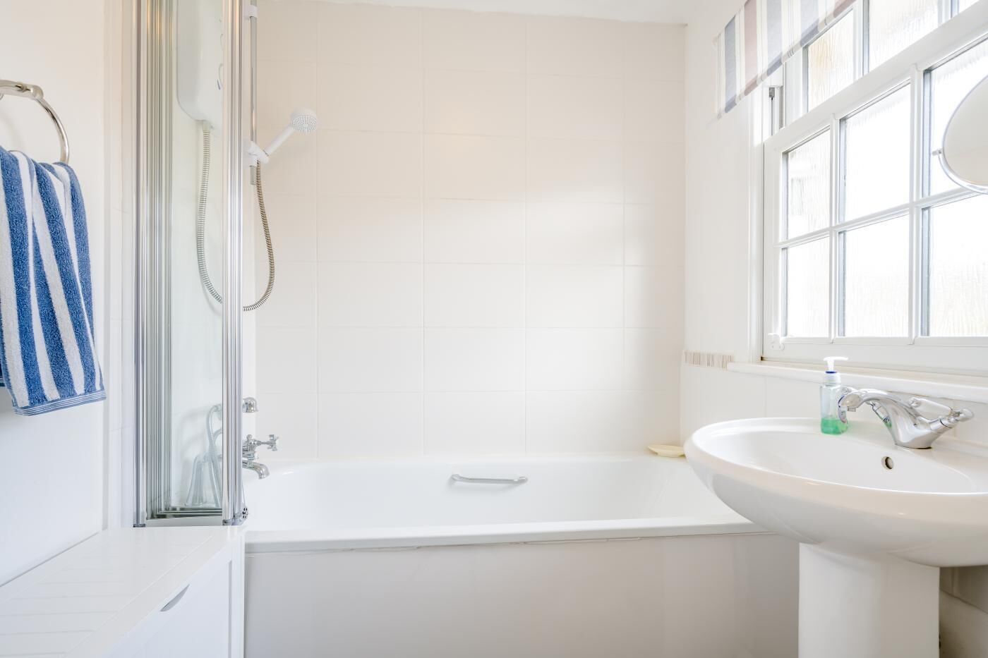 A modern bathroom with a glass-enclosed shower, a white bathtub, and a sink with a window above it.