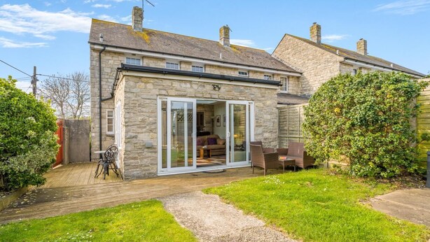 Une maison en pierre dotée d’un patio et d’une porte-fenêtre coulissante qui donne sur un intérieur comprenant un canapé et une table.