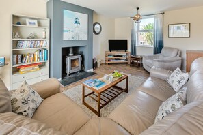 Ein Wohnzimmer mit Sofa, Couchtisch, Kamin, Bücherregal, Fernseher und einem Fenster mit Vorhängen.