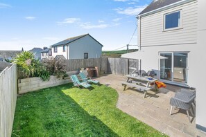 Ein Garten mit Grillplatz, zwei Liegestühlen, einem Picknicktisch und einer Schiebetür.