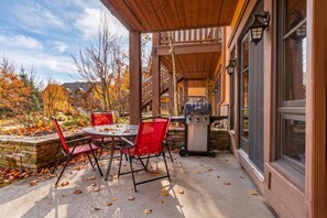 Eine Terrasse im Freien mit einem runden Tisch, Stühlen, einem Grill und einer Steinmauer.