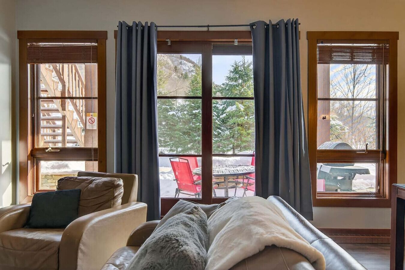 Une pièce dotée d’une grande porte-fenêtre coulissante donnant sur un espace extérieur, d’un canapé beige agr émenté d’un plaid et d’une chaise rouge visible de l’extérieur.