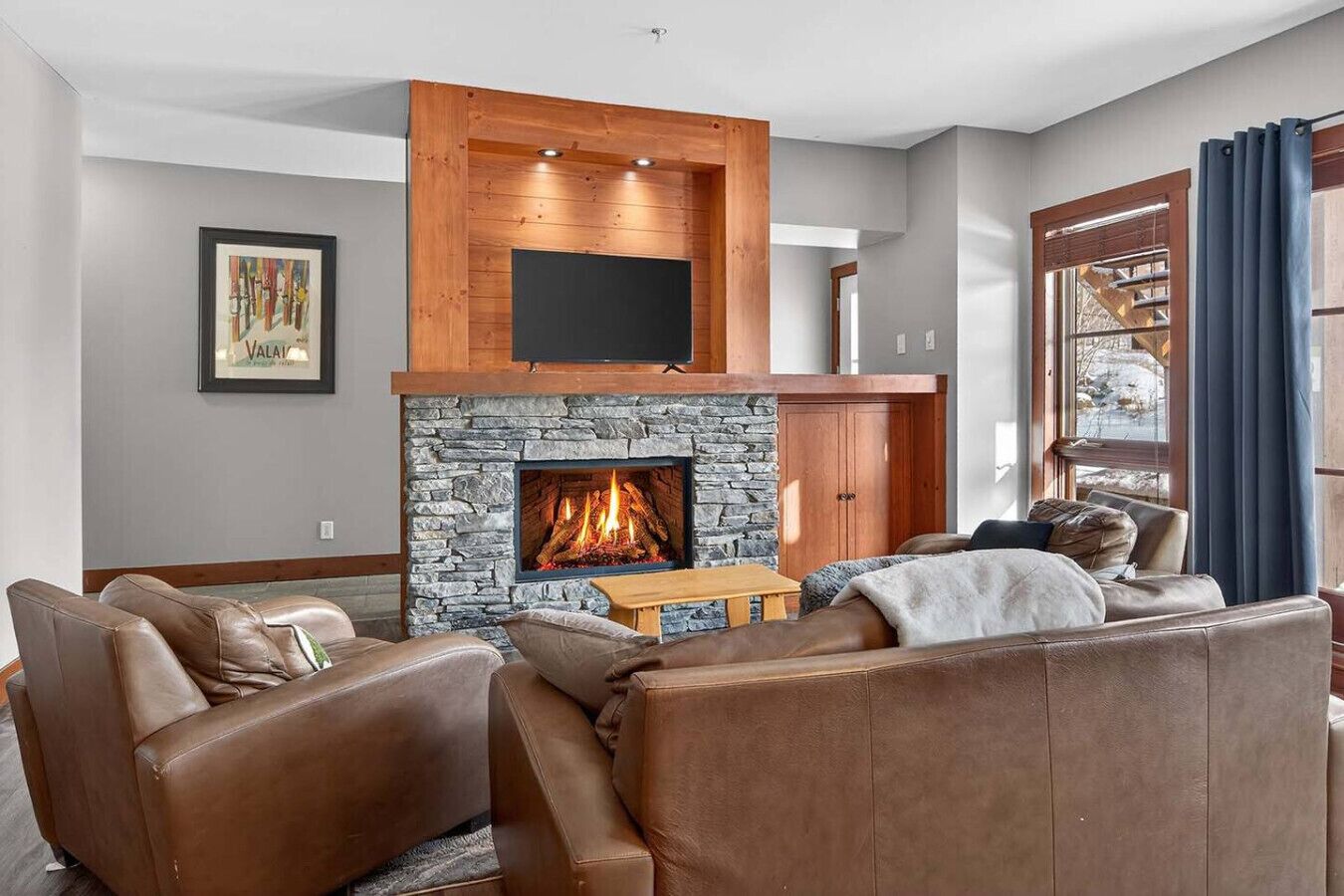 A living room with a stone fireplace, leather sofas, and a mounted TV.