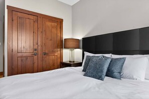 Ein Hotelzimmer mit einer großen Holztür, einem schwarzen Kopfteil und einem Bett mit weißer Bettwäsche und gemusterten Kissen.