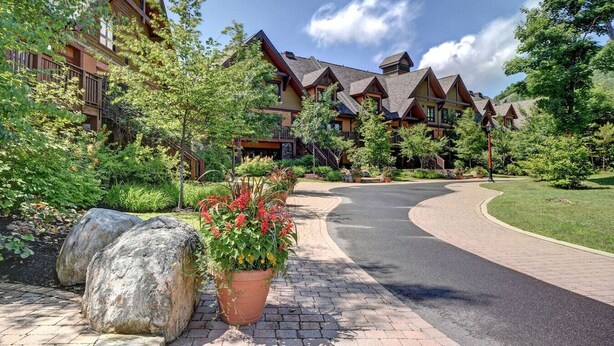 A lodge with multiple wooden cabins, a paved driveway, and a landscaped garden with large rocks and flowering plants. - Aux Étoiles EMG: Ski In/Out at Soleil Express (Mont-Tremblant)
