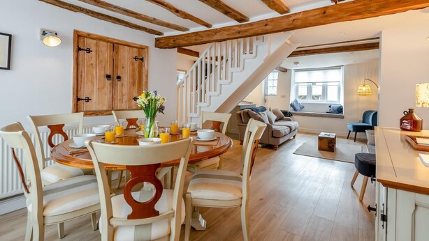 Un vaste espace dédié à la salle à manger, avec une table et des chaises en bois, un escalier menant à un niveau supérieur, et un coin salon confortable avec un canapé et des coussins.