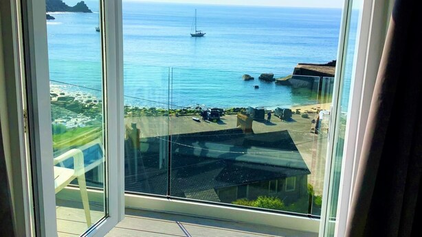 Uma varanda com vista para o mar, barcos e um litoral rochoso.