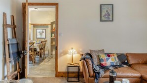 A cozy living room with a brown leather sofa, a small side table with a lamp, and a dining area in the background. - 3 Bed in Fulbeck (oc-v33643) (Fulbeck)
