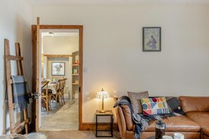 A cozy living room with a brown leather sofa, a small side table with a lamp, and a dining area in the background. - 3 Bed in Fulbeck (oc-v33643) (Fulbeck)