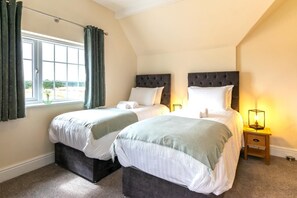 A bedroom with two beds, a window with curtains, and a bedside table with a lamp. - 3 Bed in Fulbeck (oc-v33643) (Fulbeck)