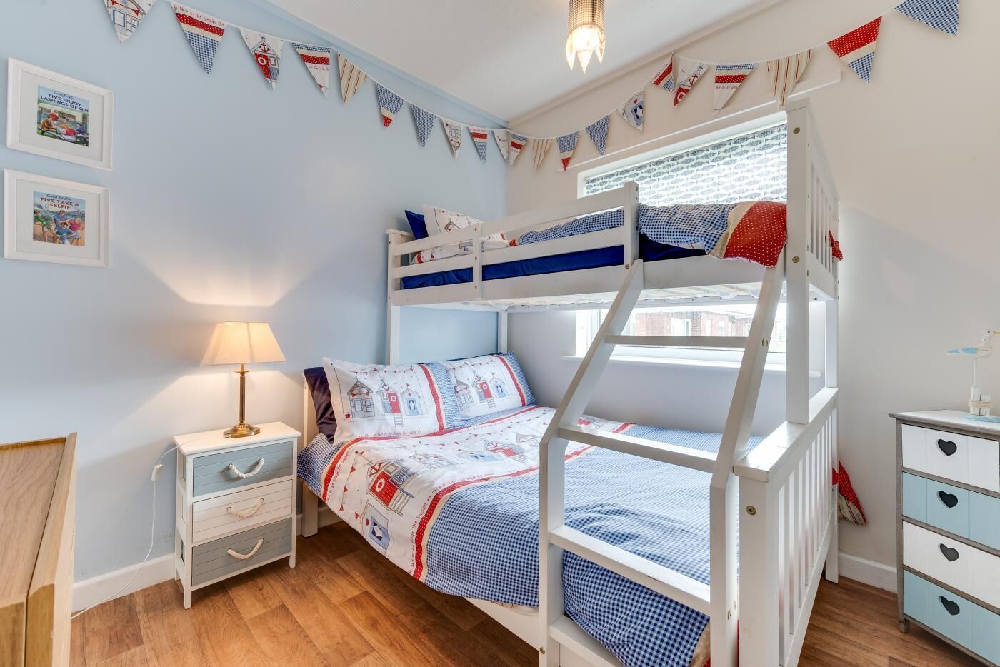 A child's bedroom with bunk beds, a nightstand, a dresser, and a window with a view.