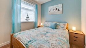 A bedroom with a bed, a nightstand, a wall-mounted lamp, a window with curtains, and a sailboat decoration. - 2 Bed in Walcott (oc-2282) (Walcott)