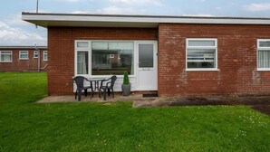 A single-story brick house with a front door, a small patio with a table and chairs, and a potted plant. - 2 Bed in Walcott (oc-2282) (Walcott)