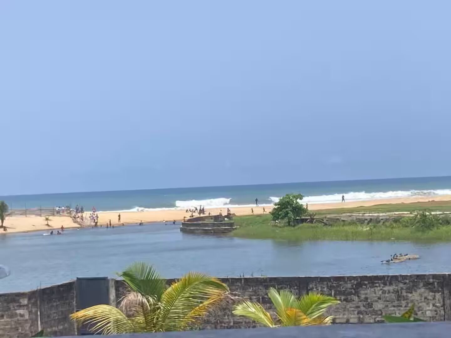 Una playa con mar tranquilo, algunas embarcaciones y gente disfrutando de la orilla.