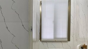 Un baño con inodoro, ventana con persianas y pared con diseño de mármol.