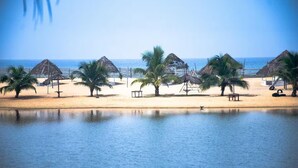 Een strand met palmbomen, hutten met rieten daken en een rustige zee.