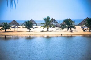 Een strand met palmbomen, hutten met rieten daken en een rustige zee.