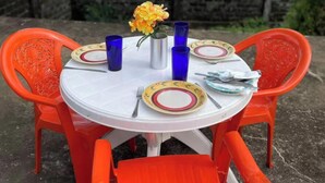 Una mesa redonda con mantel blanco, sillas anaranjadas y un florero con flores amarillas.