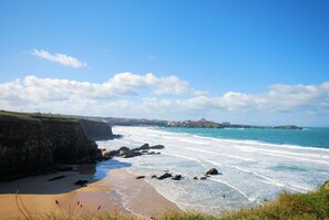 A coastal landscape with a sandy beach, rocky shoreline, and a distant view of a town. - 3 Bed in Newquay (oc-p00631) (Newquay)