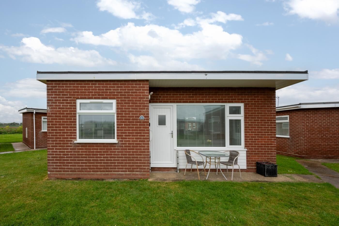 A small brick building with a white door, a window, and a small patio with a table and chairs.