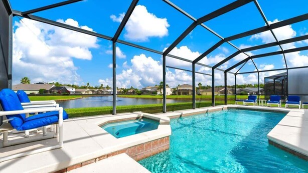 A swimming pool with a glass enclosure, blue lounge chairs, and a view of a residential area. - Poolside 5BR Escape with Pool Table & Parking (Kissimmee)
