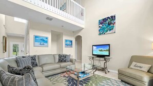 A living room with a sofa, armchair, and coffee table. There is a television on a stand and a balcony with a railing. - Poolside 5BR Escape with Pool Table & Parking (Kissimmee)