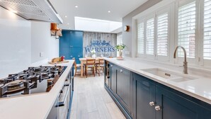 Een moderne keuken met een centraal eiland, een inbouwfornuis en een groot raam met zonwering.