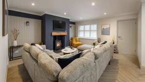 Een moderne woonkamer met een zithoek, een gele fauteuil, een open haard en een groot raam met jaloezieën.