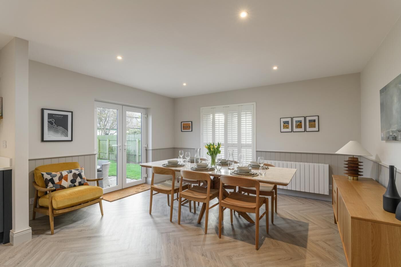 Un coin repas avec une table dressée pour quatre personnes, un fauteuil jaune et un meuble en bois.