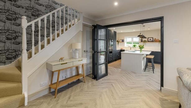 Een moderne keuken met een centraal eiland, een trap met behang met een patroon, en een zithoek met een bank.